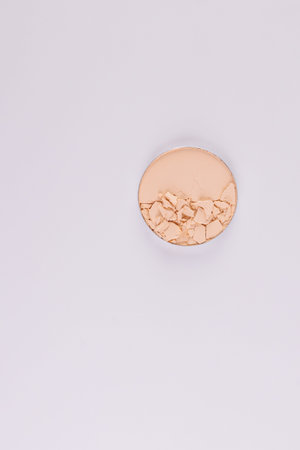 A compact powder in a natural beige color in a round block with broken pieces of texture. Top view....