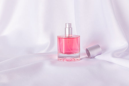 A chic bottle of women's perfume or cosmetic spray against a background of white satin folds. Front...