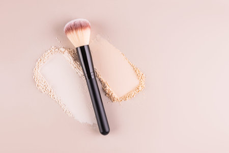 Two samples of loose powder in different tones and a makeup brush on a beige background. Top view. A...