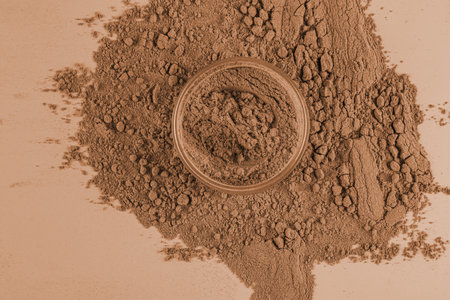 An open jar of loose powder in a bronze tone for dark skin on a background of a lot of loose texture. The concept of decorative cosmetics.の写真素材