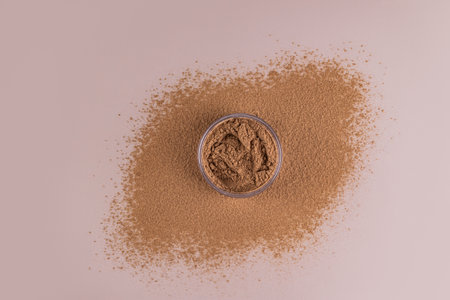 Cosmetic jar with loose powder bronze tone for dark skin or tanned skin stands on loose powder. top view. sample texture of the productの写真素材