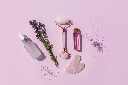 lavender oil for massage and skin care of the face and body, roller massager, gua sha, lavender salt on a lilac background. top view. flat layの写真素材