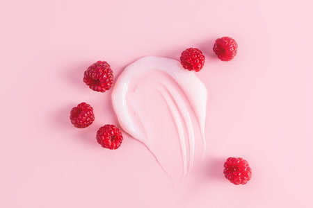 smeared soft pink, transparent lip balm sample and ripe raspberries on a pink background top view. A copy space. lip care. cosmetic smearの写真素材