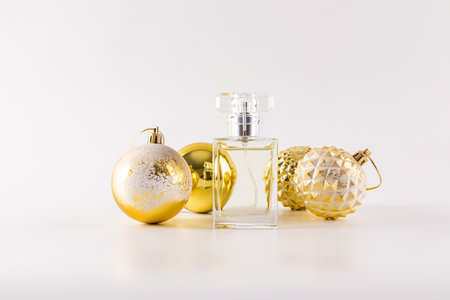 An elegant bottle of perfume stands between New Years snow-covered golden balls on a white background. Front view. New Years product, fragrance.の写真素材