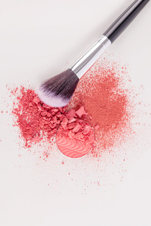 A beautiful makeup brush is lying on a sample of dry scattered blush in a pink tone on white background. The top vertical view. decorative cosmetics.の写真素材