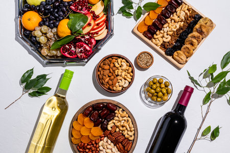 Traditional treats for the Tu bi shvat holiday on white background. trays with dried fruits, nuts, olives, bottles red and white wine. view. flat layの写真素材