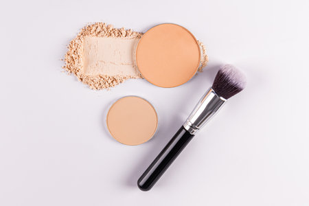 Two round blocks of compact powder in a natural tone, a sample of dry powder and a professional makeup brush on a white background. cosmetic conceptの写真素材