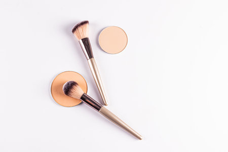 Two blocks, refills of compact powder in a light tone, a makeup sponge, two brushes on a white...