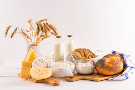 Homemade cottage cheese, cheese, bread, bottled milk, a vase with spikes on a white wooden table. still life for the holiday of Shavuot. Front viewの写真素材