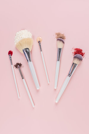 A set of chic white professional makeup brushes on a pink vertical background with color cosmetics...