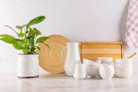 Beautiful kitchen background with a set of white ceramic utensils, wooden cutting boards, green houseplant in a stylish pot. Front view.の写真素材