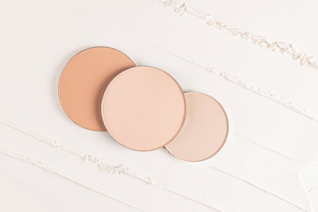 Three cosmetic blocks, a refill of different tones of compact powder on a light background of loose powder. Beautiful cosmetic background. layoutの写真素材
