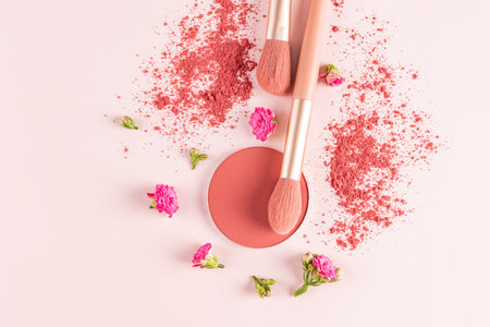 Round refill of pink blush and two makeup makeup brushes on a pink background with flowers among the scattered blush. decorative cosmetics. top view.の写真素材