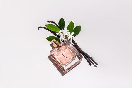 A chic bottle of perfume with a floral vanilla scent lies on a white background with vanilla sticks and delicate flowers. A blank bottle mockupの写真素材