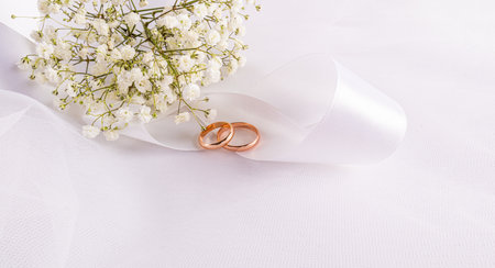 Chic wedding banner with two gold wedding rings lying on a spiral of white satin ribbon and a bouquet of gypsophila. wedding concept. A copy spaceの写真素材