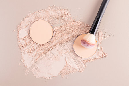 Two round blocks of compact powder in a natural tone lie on a sample of scattered powder with a makeup brush. cosmetic background. texture sampleの写真素材