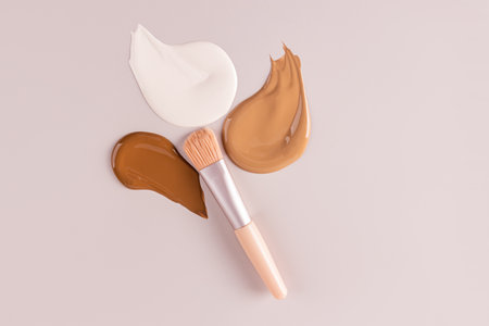 Three chic cosmetic strokes of foundation powder in different tones on a pastel background with a makeup brush. Samples texture liquid base. top viewの写真素材