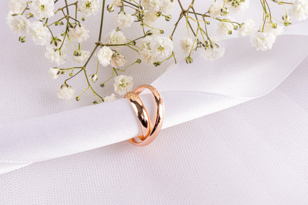 Two gold wedding rings are strung on a white satin ribbon on a white fabric background with a chic gypsophila. A copy space. postcard, invitation.の写真素材