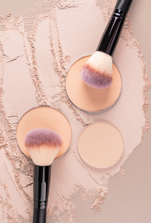 Three blocks of natural tone round compact powder on a scattered dry powder texture with professional makeup brushes. The top vertical viewの写真素材