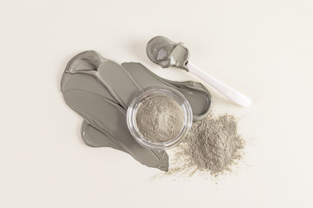 Dry natural clay powder of gray in a glass bowl is on smears of liquid cosmetic clay texture, mask. The ceramic spoon is filled with clay. top view.の写真素材