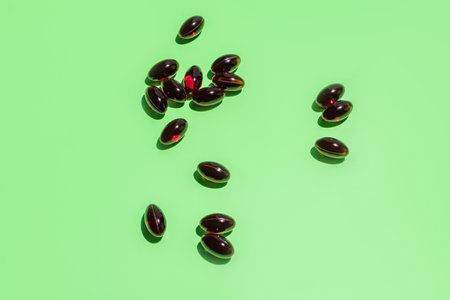Red oval capsules with vitamin E are scattered on a green background. The concept of additional nutrition of the skin, hair, heart. top view.の写真素材