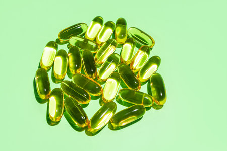 Golden gelatin capsules folded in a circle, natural omega fatty acid oil on a green background....