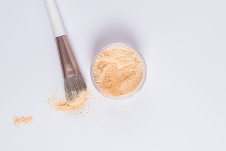Open cosmetic jar with natural tone dry powder on a white background with makeup brush. Upper view....