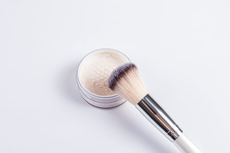 A fluffy cosmetic makeup brush lies on an open jar with dry powder in a light tone. Professional dry...