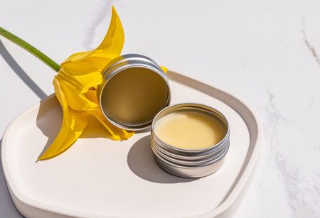 Two Round Cosmetic Metal Jars with Natural Balm, Lip Care Oil on a White Yellow Tulip Tray. Gentle care. Front view. A natural cosmetic productの写真素材