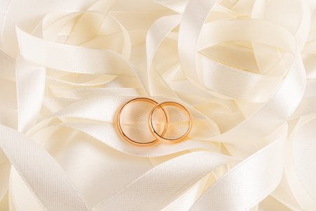 Top view of two gold wedding rings lying on a beige pile of satin ribbons. A copy of the space. Wedding mockup for card design, invitationの写真素材