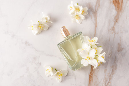 An elegant bottle of cosmetic spray lies on an abstract marble background with white jasmine...