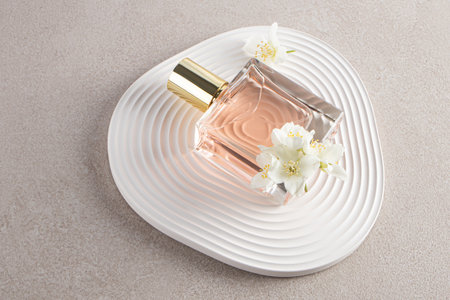 A transparent bottle of women's perfume with a delicate scent of jasmine lies on an abstract relief podium with jasmine flowers. Beautiful still lifeの写真素材