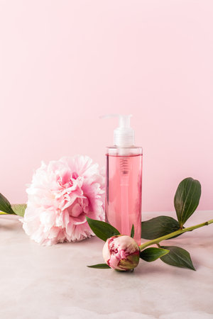 Cosmetic transparent bottle packaging dispensary with a gentle product for spa treatments. Pink vertical background with live peonies. A copy spaceの写真素材