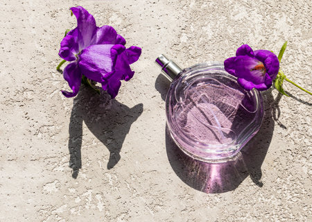 bottle of women's perfume with floral fragrance on a gray cement background with bright flowers. the...