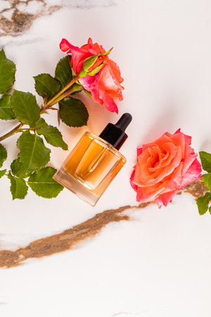 A natural beauty product in a clear dropper bottle on a marble abstract background among pink roses. vertical top view. A blank bottle mockupの写真素材