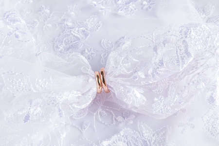 Two gold wedding rings are worn on the chic openwork fabric of a dress or white veil. Top view. A...