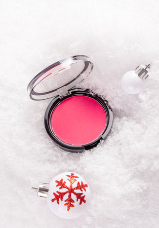 Open pack of pink blush on white fluffy snow among Christmas balls. Product presentation. layout. New Year's concept of decorative cosmeticsの写真素材