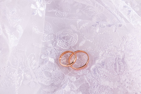 A pair of gold wedding rings on a white openwork background of the bride's dress. Beautiful wedding card mockup, invitation. top view. A copy space.の写真素材