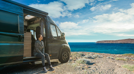 Woman sitting on the side of camper van looking at the seaの写真素材
