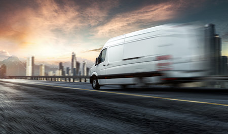 White commercial delivery van on the road with cityscape in the backgroundの写真素材