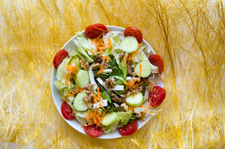 Dish of mix salad on yellow background with cucumbers, walnuts, tomatoes, carrots, lettuce, fetaの写真素材