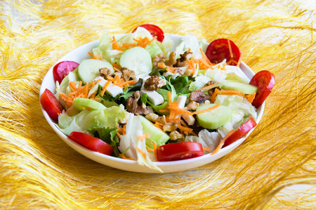 Dish of mix salad on yellow background with cucumbers, walnuts, tomatoes, carrots, lettuce, fetaの写真素材