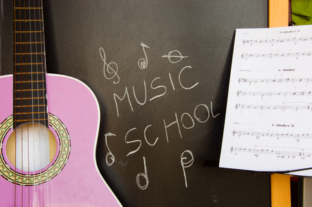 Music school for children with purple guitar closeup on blackboard background and music sheetsの写真素材