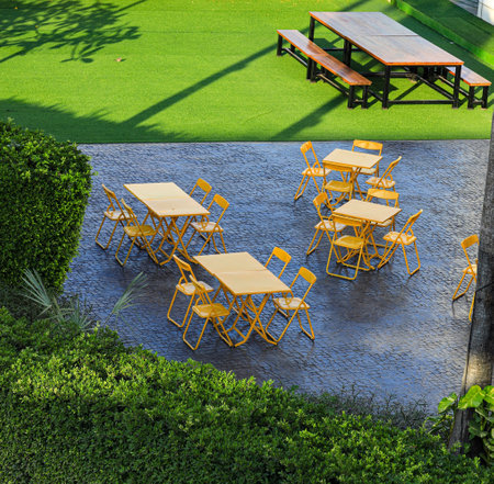 Sets of yellow metal table and chairs in the courtyard. Dining table in the park Surrounded by green vegetation.の写真素材