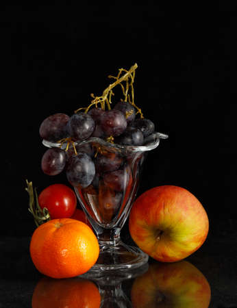 Grapes in ice coupe surrounded by other fruits against a black background and with some reflections on the bottom.の写真素材