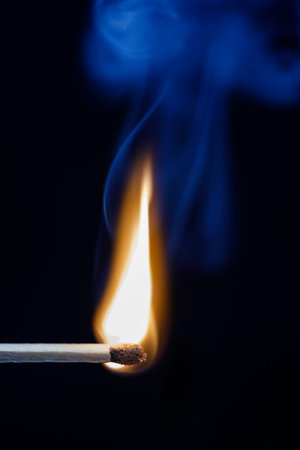 Just lit matchstick with blue smoke rising in the air against a black background