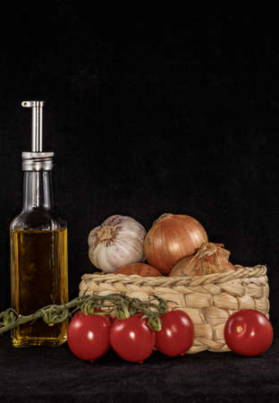 Olive oil alongside a basket with garlic, onions and tomatoesの写真素材