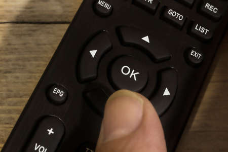The thumb presses the OK button on the remote control. It can be used as a symbol of readiness for action, a change of scenery. Selective soft focus.の写真素材