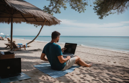 Young man working on laptop while sitting on the beach in the morningの素材