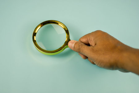 Close-up of a magnifying glass, highlighting its golden frame against a light teal background.の写真素材